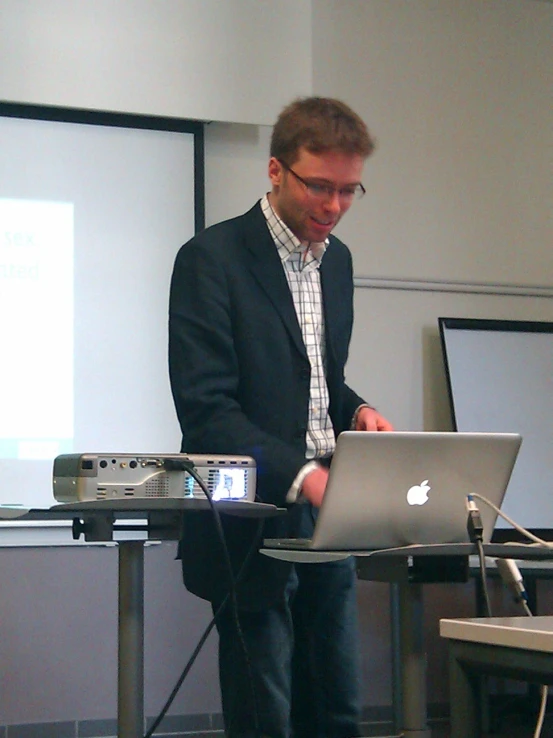 a man in glasses standing in front of a lap top