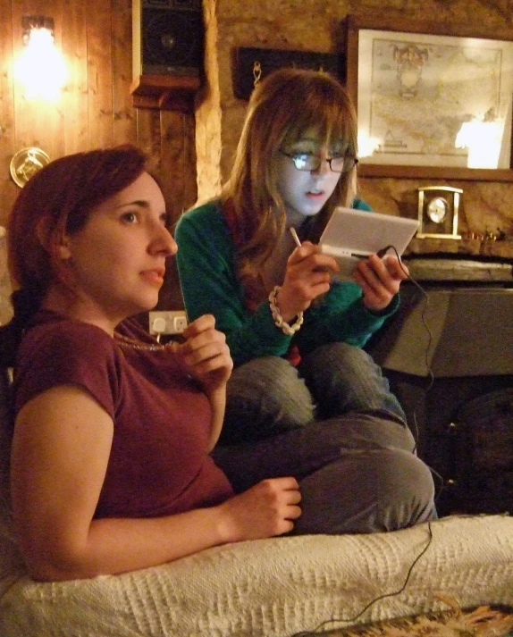 a girl sitting next to another girl and using her device