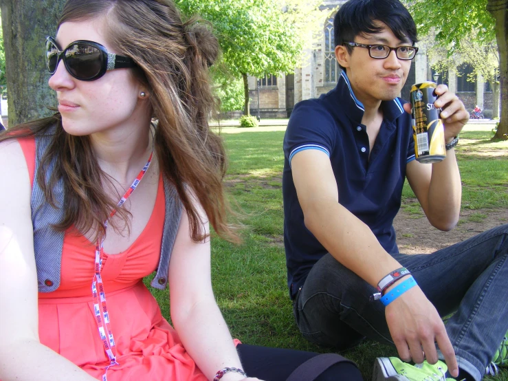 man and woman in sunglasses are sitting on grass with beer