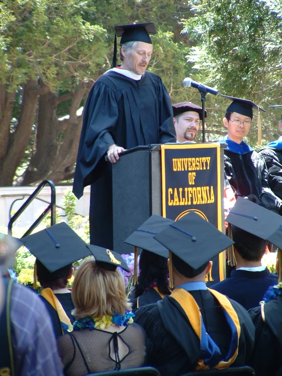 students in graduation robes with professor and speaker at graduation