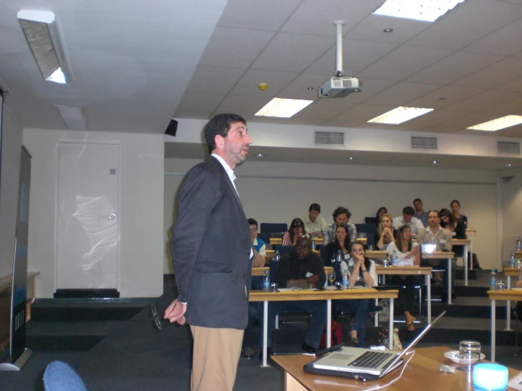 a man is standing at a desk in front of many students