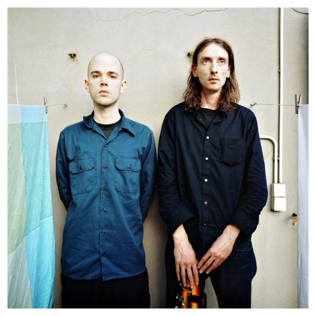 two young men standing next to each other, with one holding a bottle