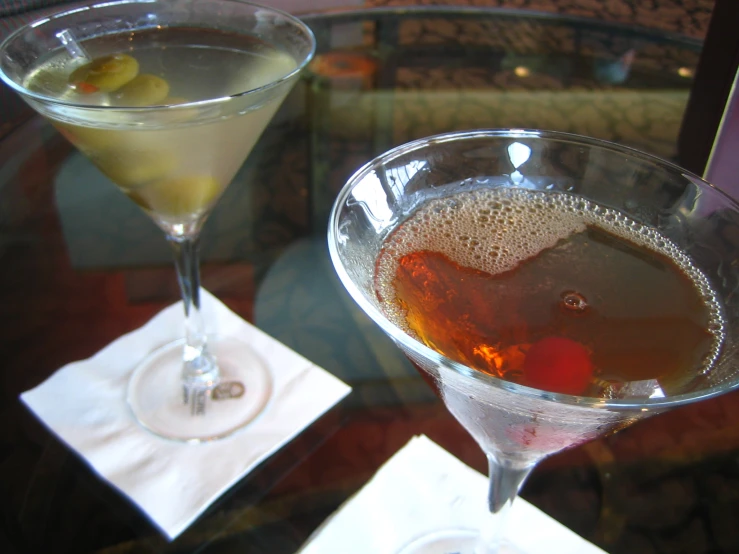 two drinks in martini glasses sit side by side on top of a table