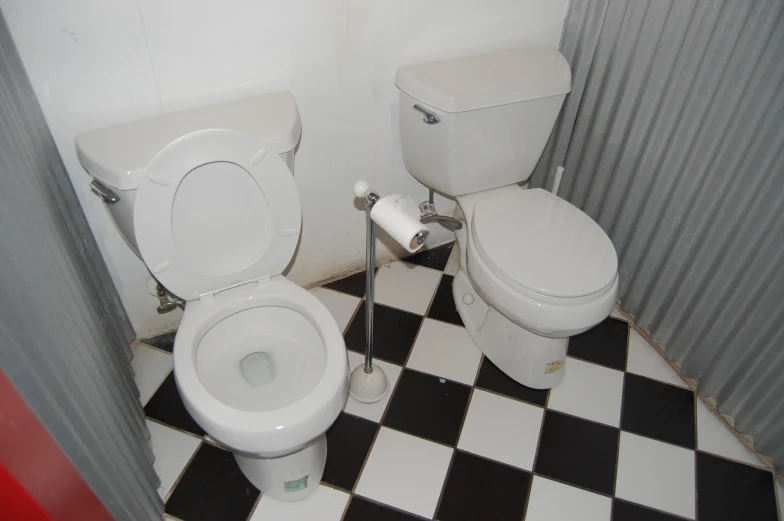 a bathroom with two toilets sitting side by side on checkered tile flooring