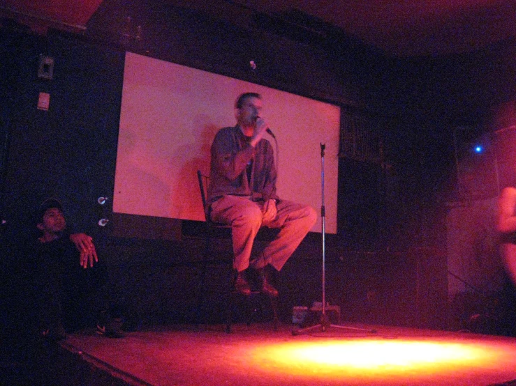 people sitting at a table while one stands on a stage while a person in the dark is standing up