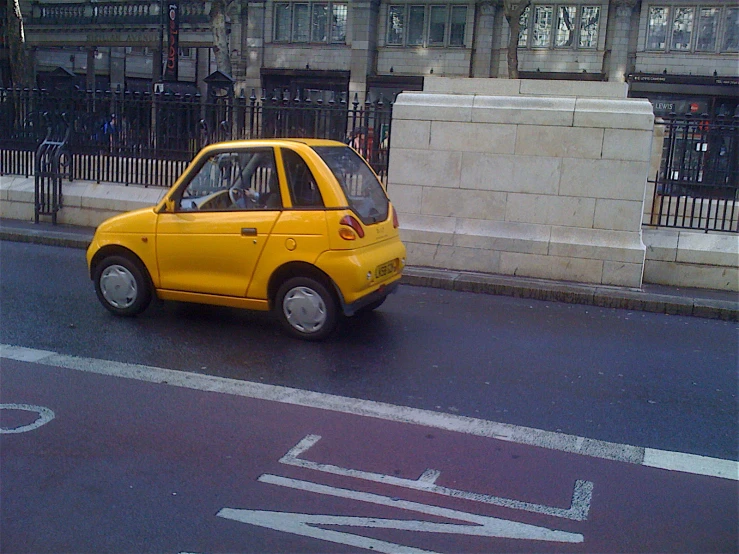 a yellow small car drives down a street