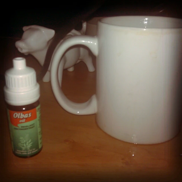 there is a white coffee mug on a wooden table next to a bottle