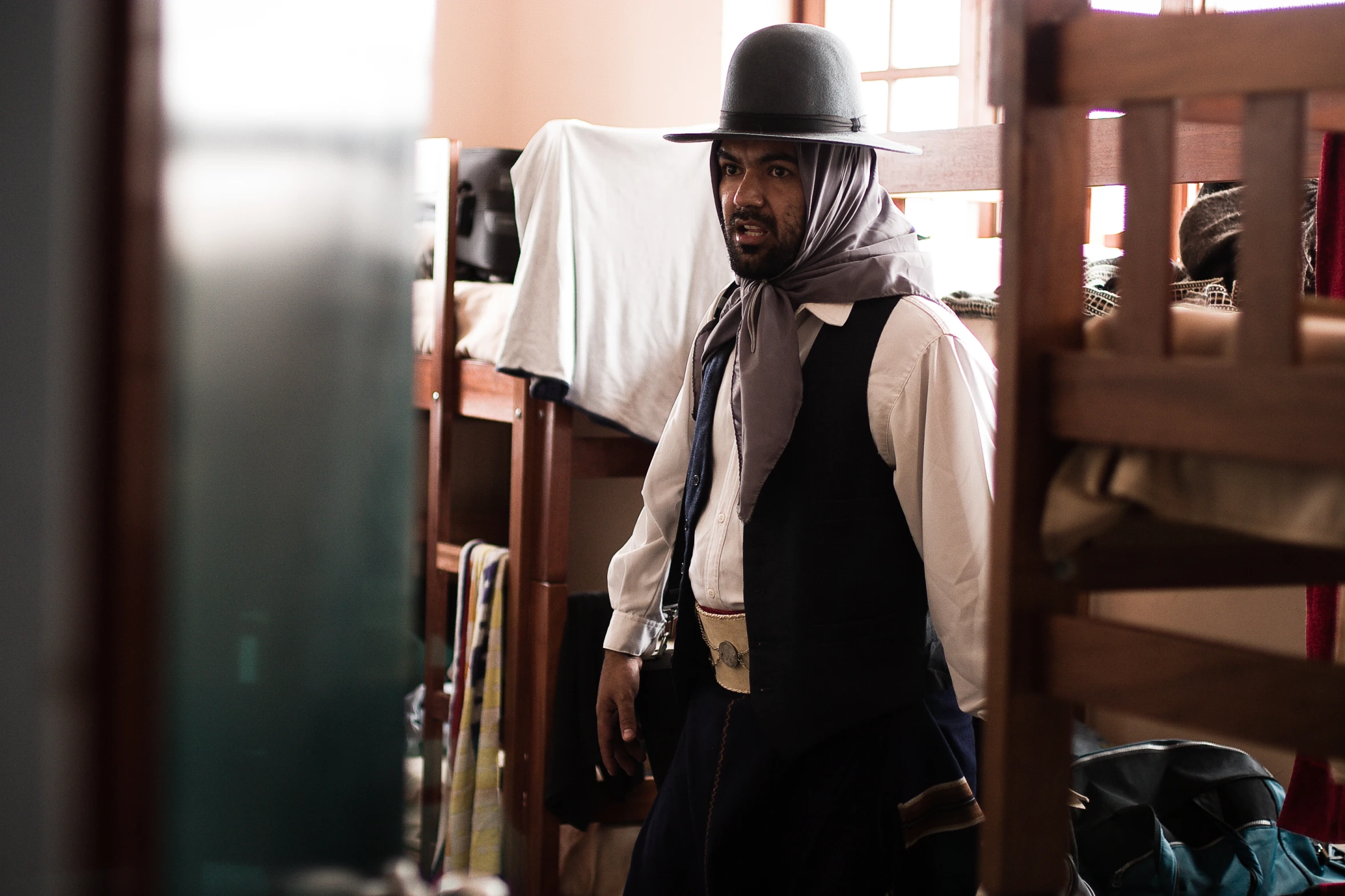 a man wearing a hat and tie in a room with bunk beds