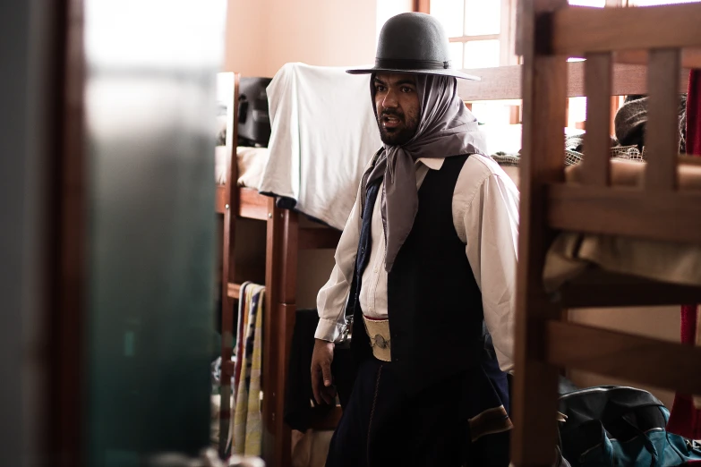 a man wearing a hat and tie in a room with bunk beds