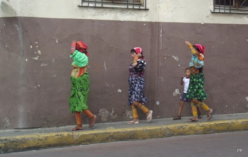 four women walking on the street near a wall