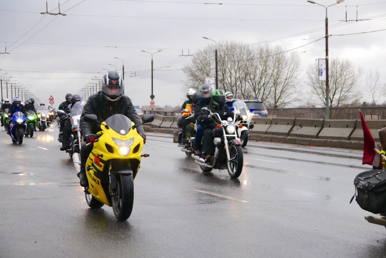 several men on motorcycles driving down a road in the rain