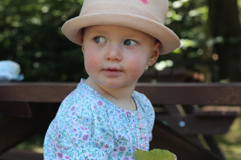 an adorable little girl sitting on top of a wooden bench