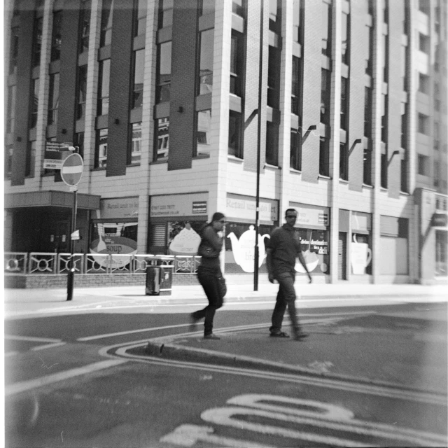 two men walk across a street in front of a big building