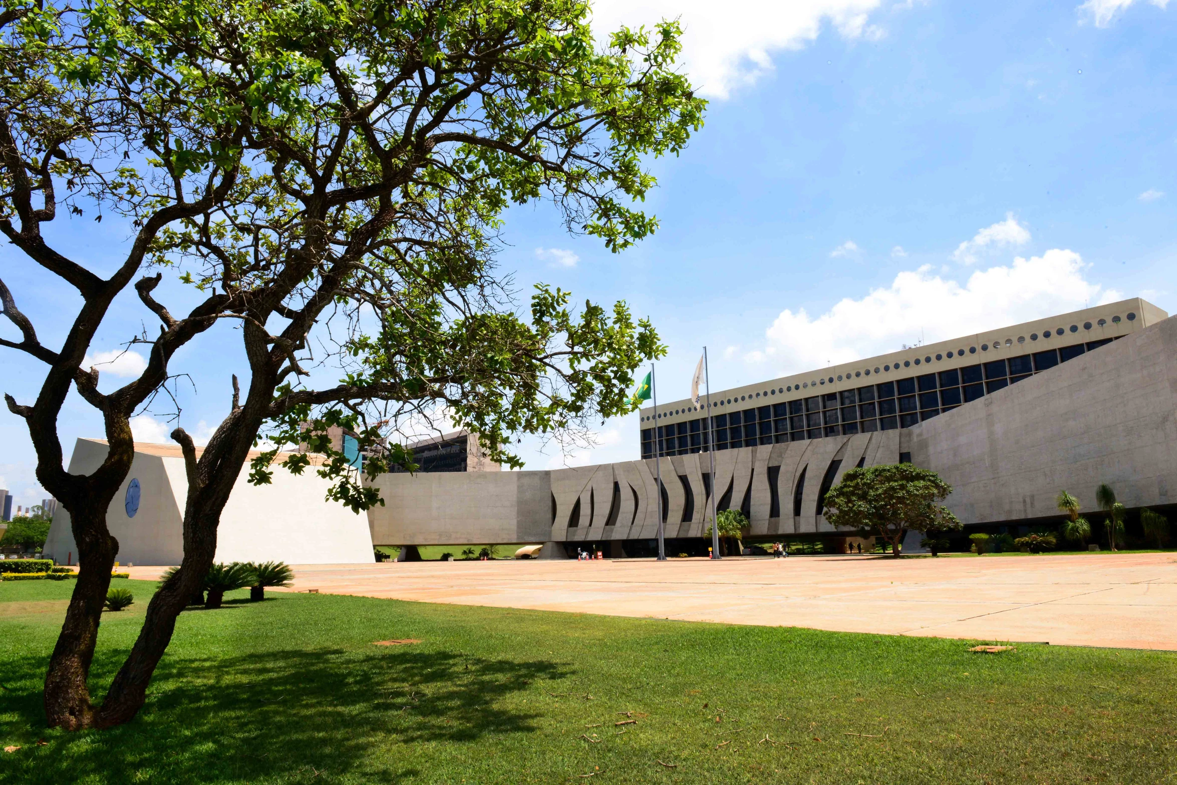 a large building sitting in the middle of a park with a tree next to it