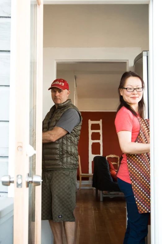 two people stand in the doorway, one wearing a vest and tie, while the other with glasses on