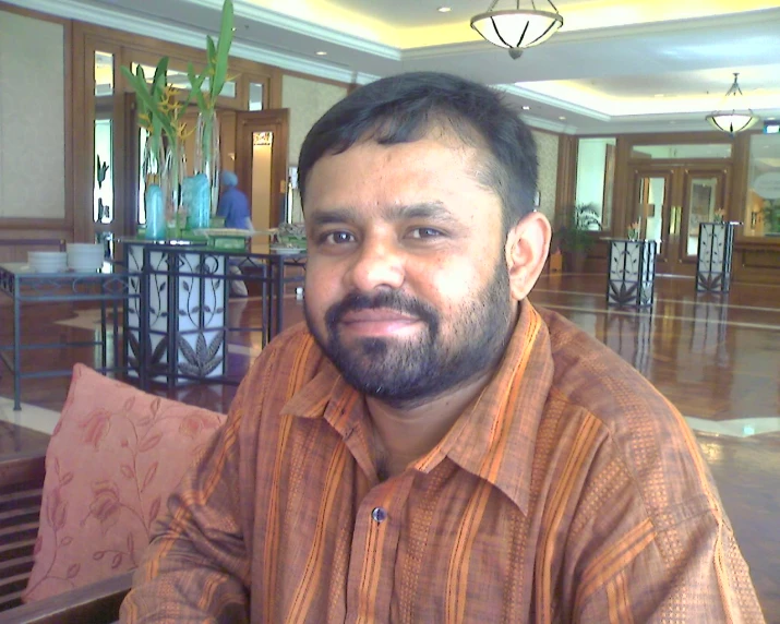 man with beard in orange striped shirt sitting on the edge of an indoor deck area