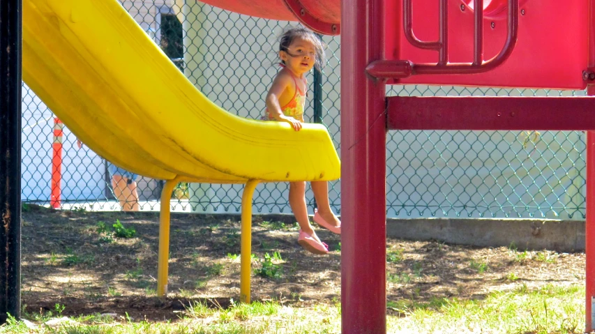 there is a small girl sitting on top of a yellow slide