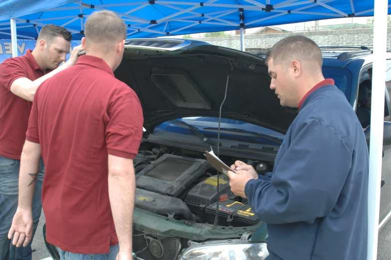 three men standing next to an open hood car