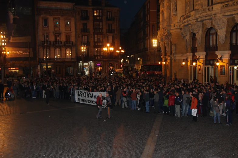 many people stand outside of an old building in a dark lit street