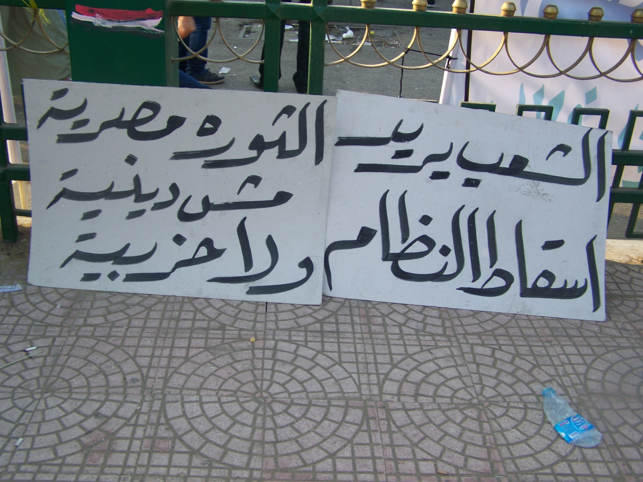 two square - sided posters with writing on them are taped to a metal post