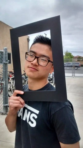 a man with glasses holding up a black framed picture