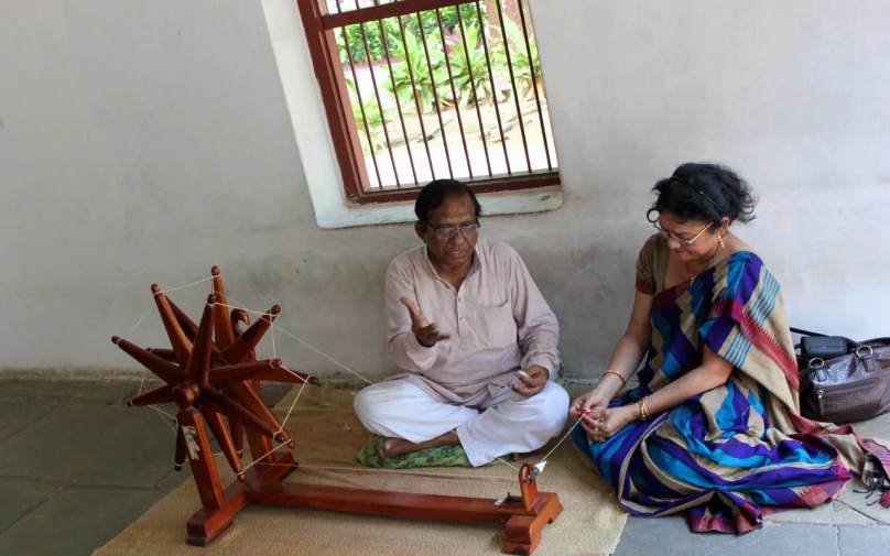 man and woman sitting down on floor weaving a piece of wood