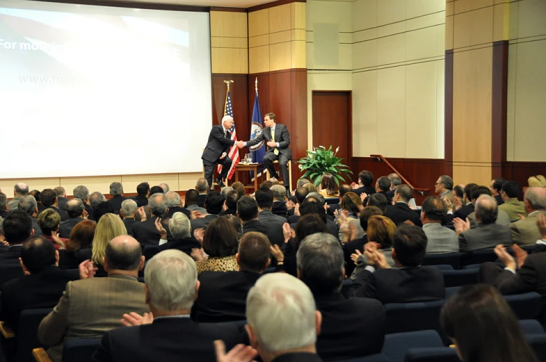 a large crowd watches a panel at an event