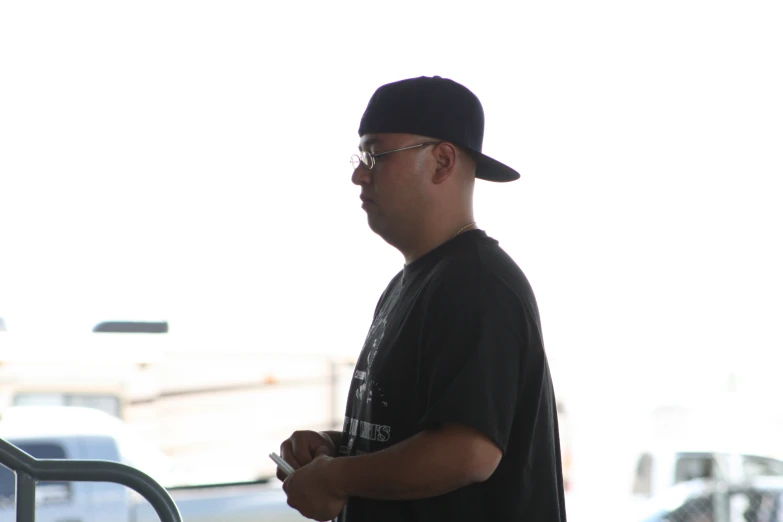 a man wearing glasses, a black shirt and a cap stands by a railing