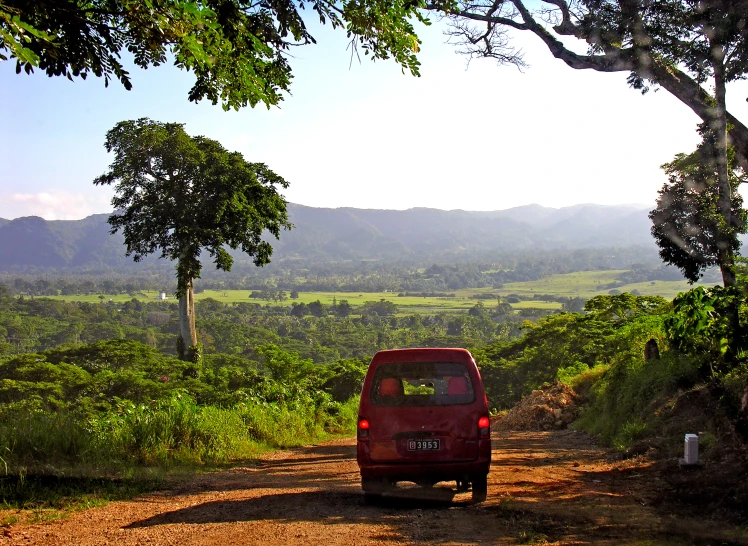 a red car is on the side of a dirt road