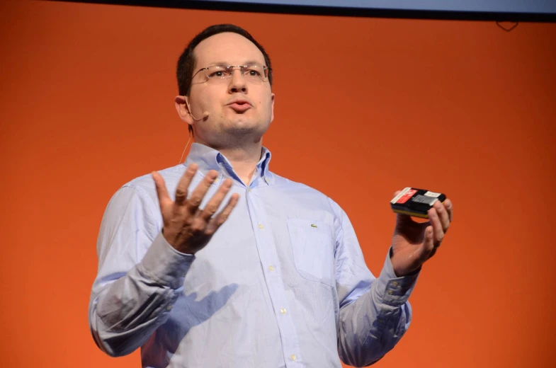 a man in glasses holds up a cell phone