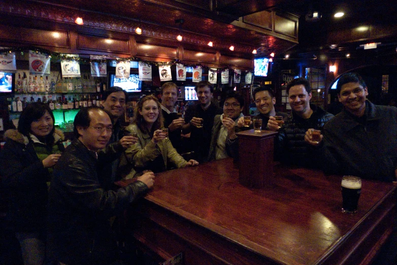 a group of friends is sitting at the bar drinking beer