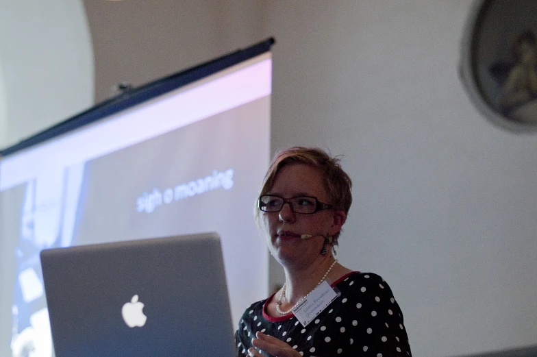 a woman in front of an apple laptop talking to someone