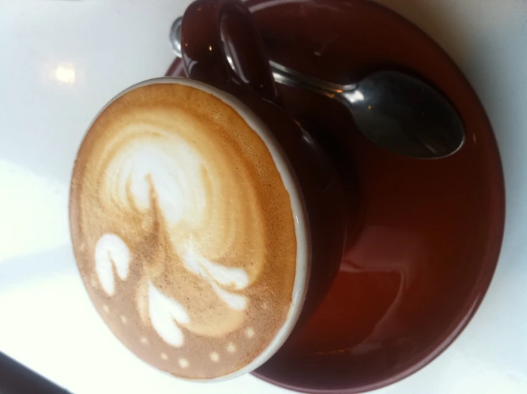 cappuccino on saucer with spoons sitting on white table