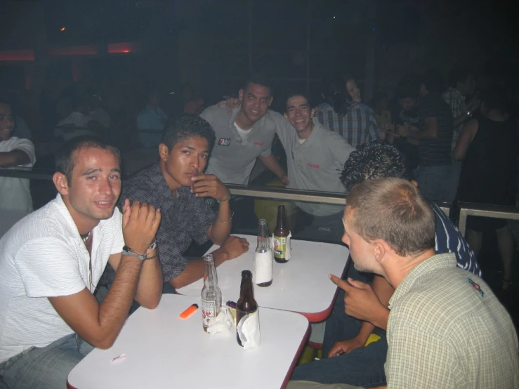 four men smiling and sitting at tables with drinks in front of them