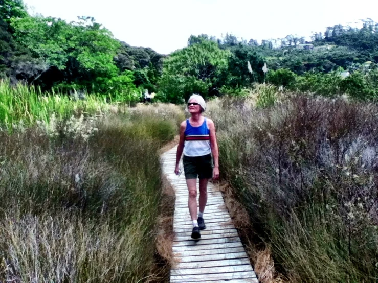 a woman is standing on the side of a boardwalk in a field