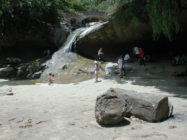 there are many people standing on the rocks beside a waterfall