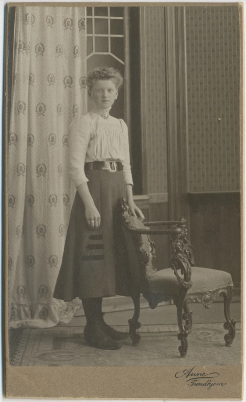 a little girl with a white shirt and hat is standing in front of a chair