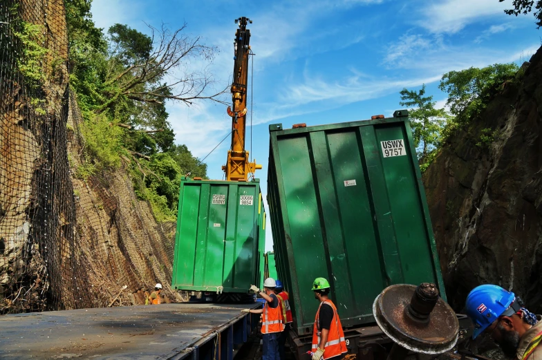 some men standing next to green containers by the rocks