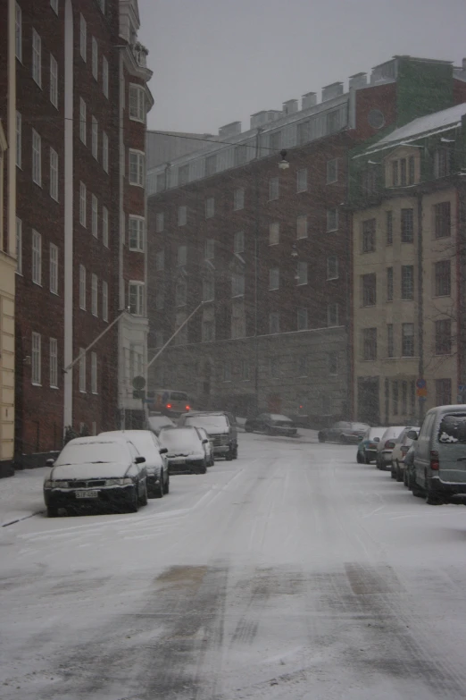 a snowy street full of parked cars and buildings