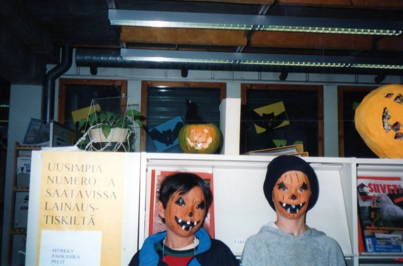 two children in orange costumes stand by halloween pumpkins