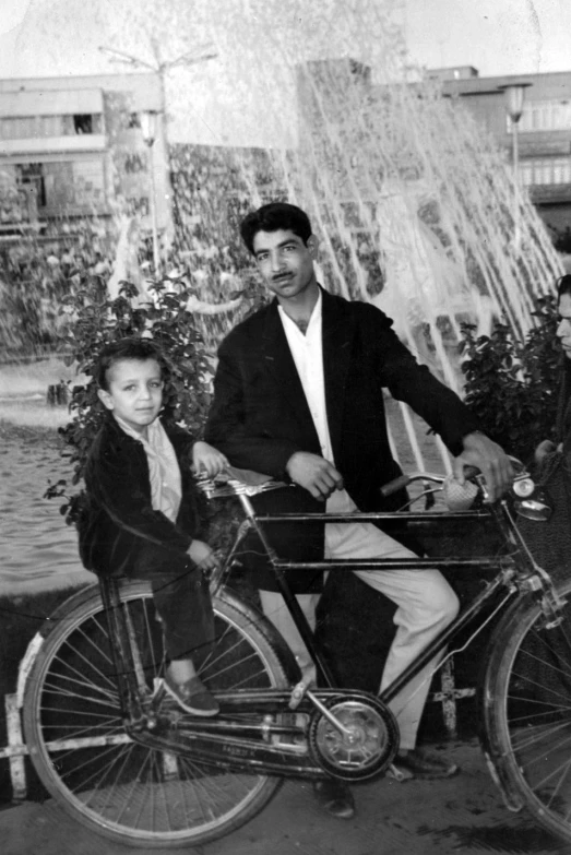 an old black and white po with an older man hing a bicycle next to a little girl on her lap