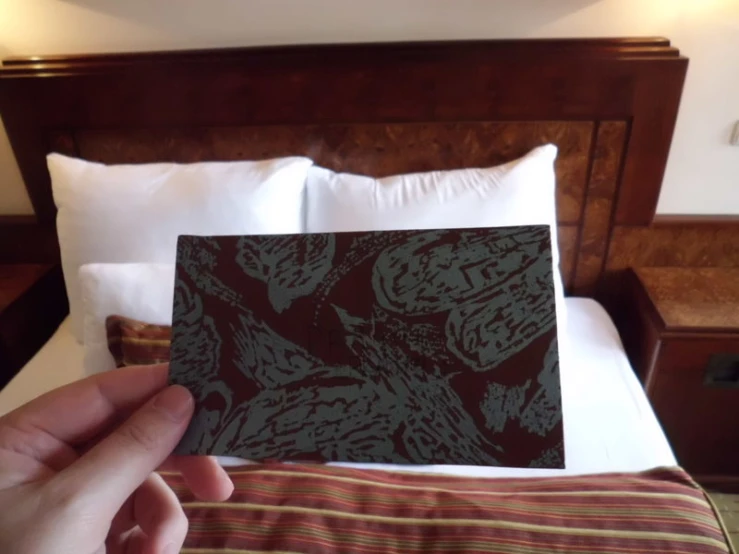 someone's hand is holding the small square card on a bed