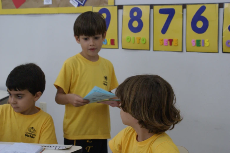 three children in yellow shirts standing at desk in a room