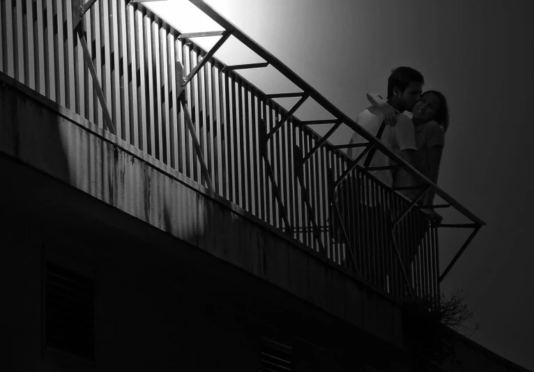 a man and woman kissing on top of a balcony