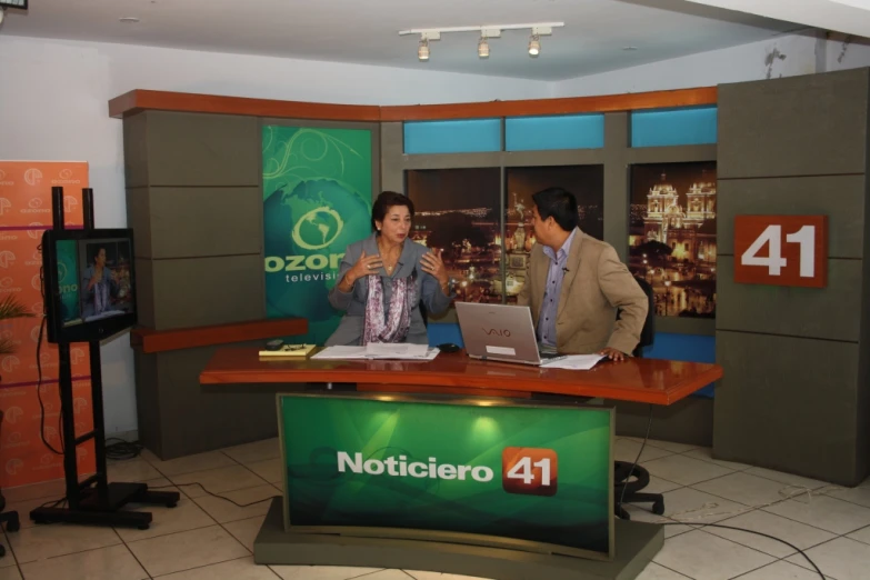 two people on desk with two television sets in background
