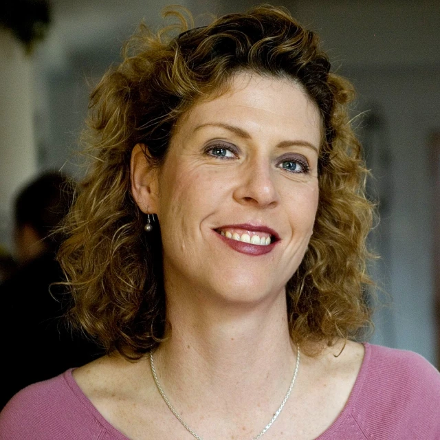 a woman with brown curly hair wearing a purple shirt