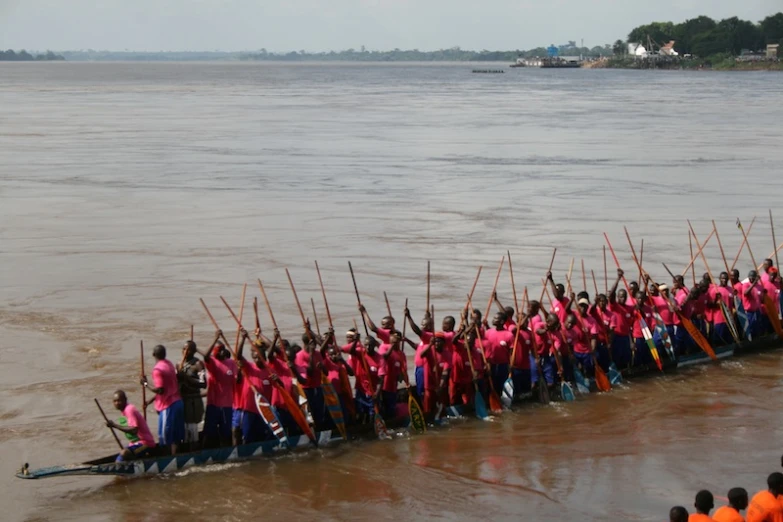 a long boat is being hed across the water by people in red shirts