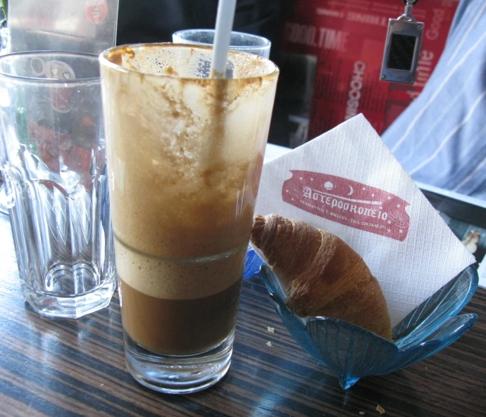 a cup of coffee with cream, some croissant and a drink next to it