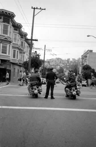 two motorcycles are stopped at the corner while some riders stand