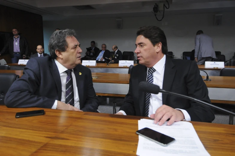 two men sit at a table in front of microphones